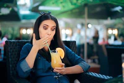 woman with hand over mouth holding glass of orange juice