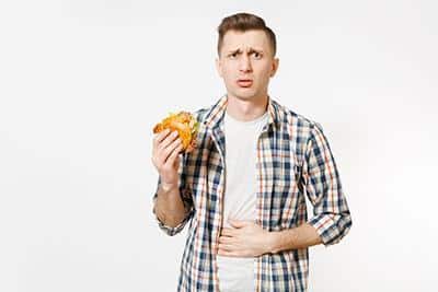 man holding sandwich and experiencing stomach pain